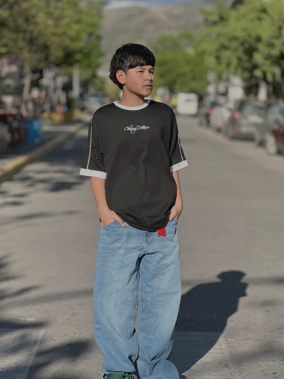 Chico de pie en la calle peatonal de La Falda, con remera negra de mangas con vivos blancos y jean ancho